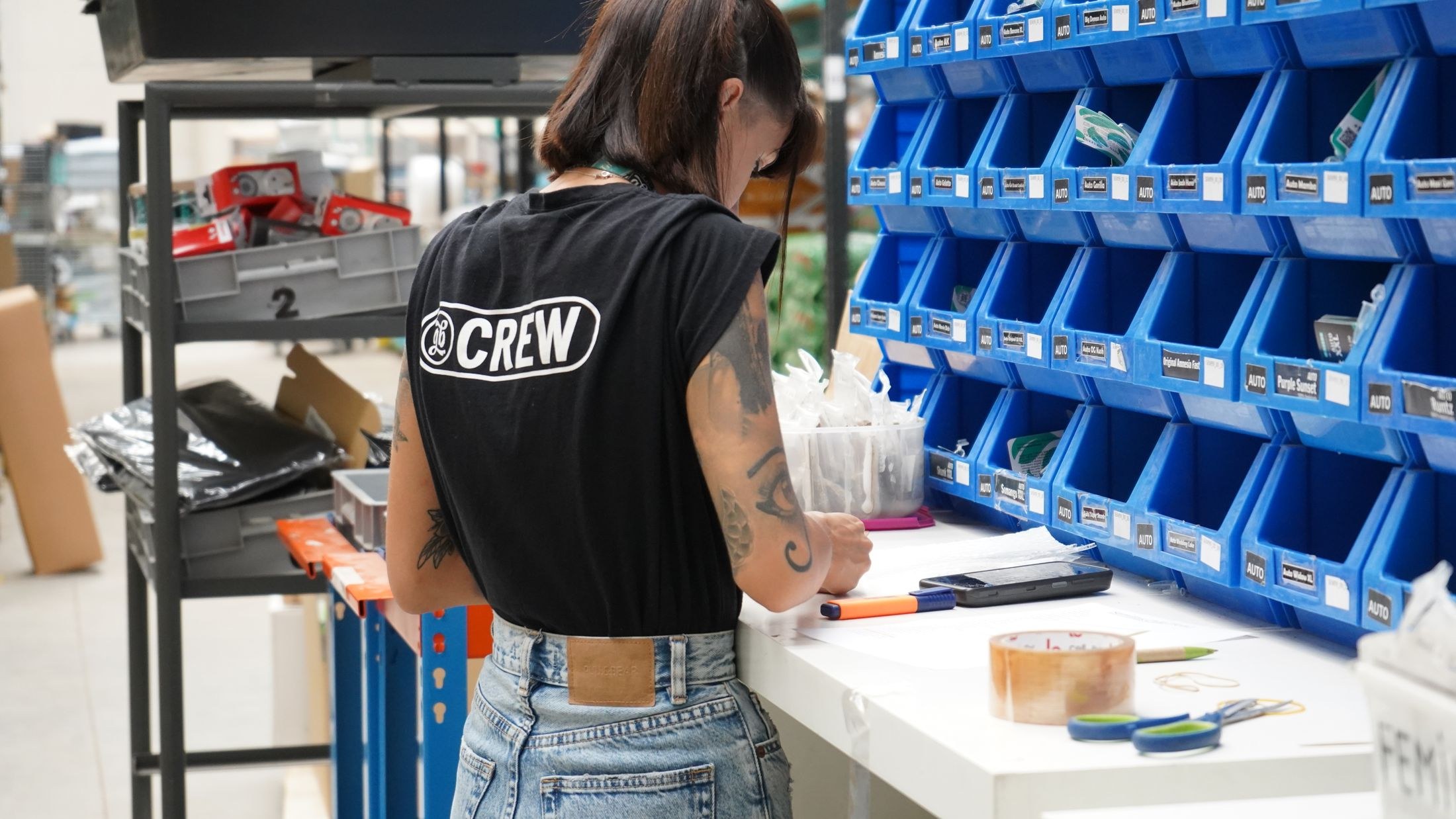 Warehouse worker checking paperwork at a packing bench beside blue inventory bins